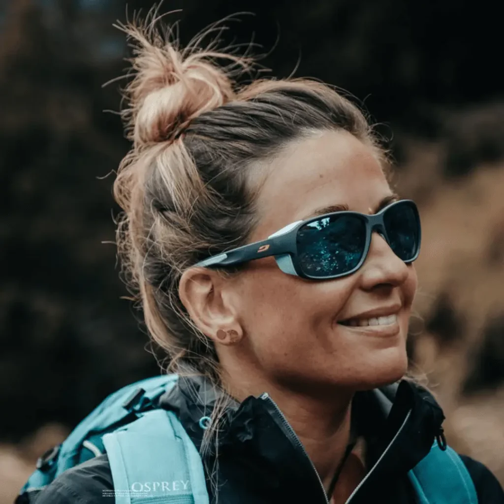 Frau mit Sonnenbrille Monterosa von Julbo und Rucksack lächelt outdoors.