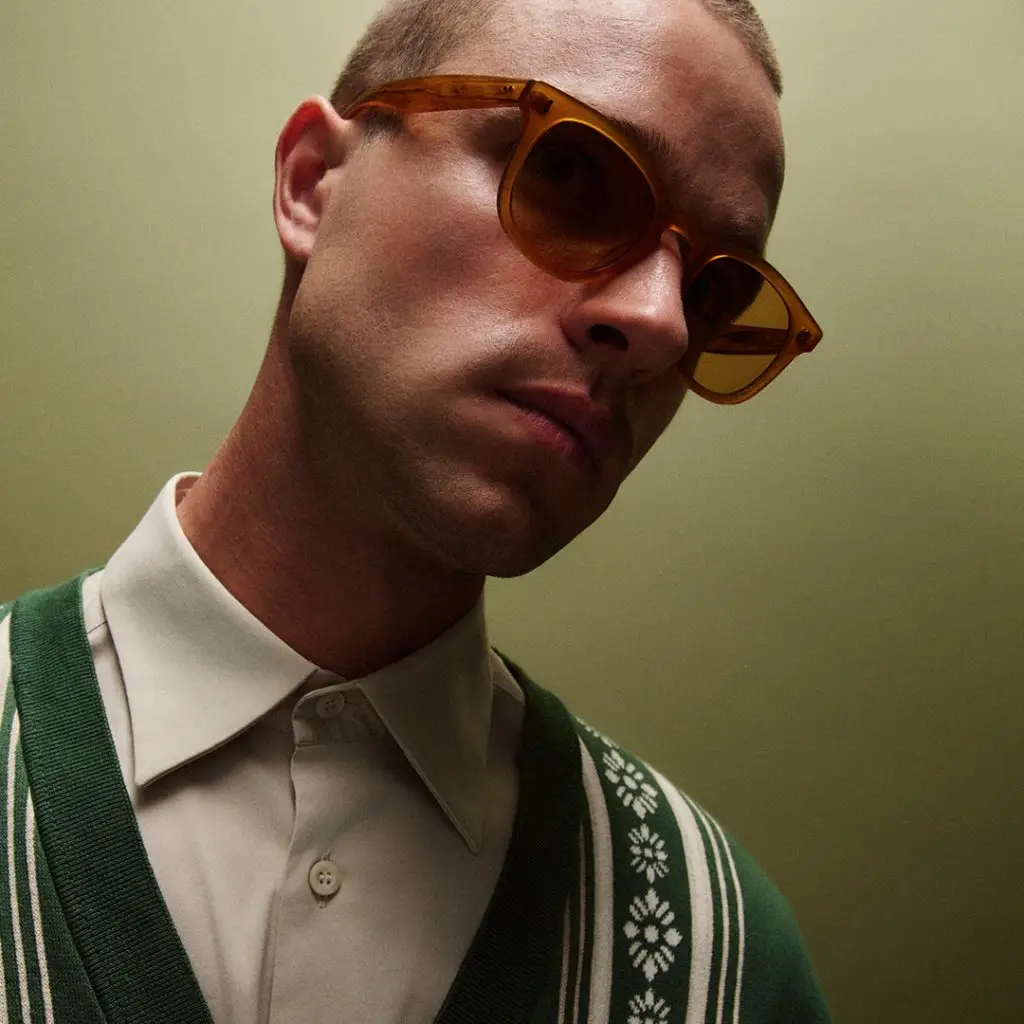 Mann mit Sonnenbrille Kenney von GLCO und Retro-Pullover.