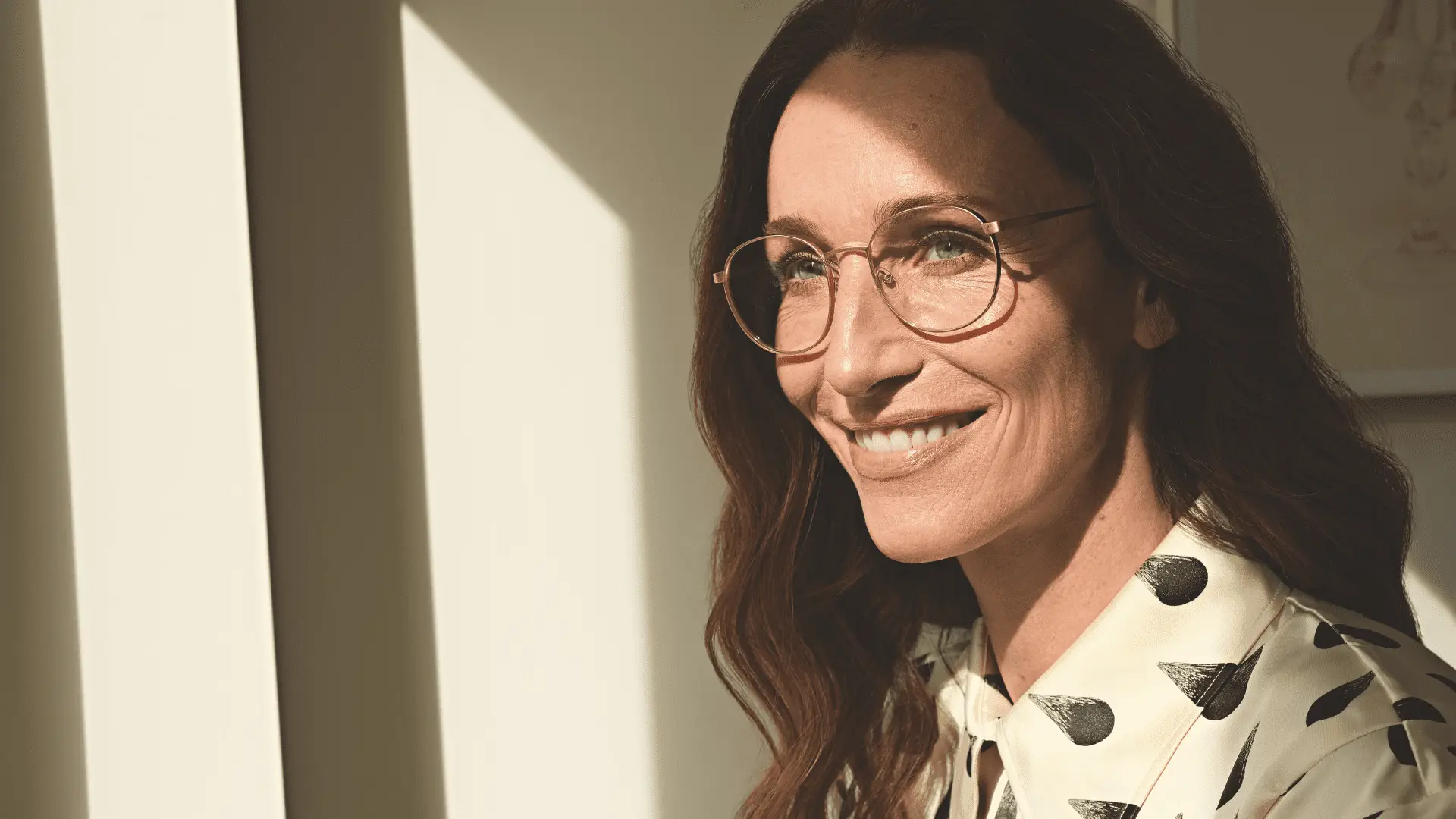 Frau mit feiner Götti Brille lächelt gegen Licht.